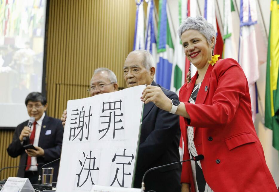 「謝罪決定」と書かれたボードを持つブラジル政府の恩赦委員会のアルメイダ委員長（右端）＝25日、ブラジリア（共同）