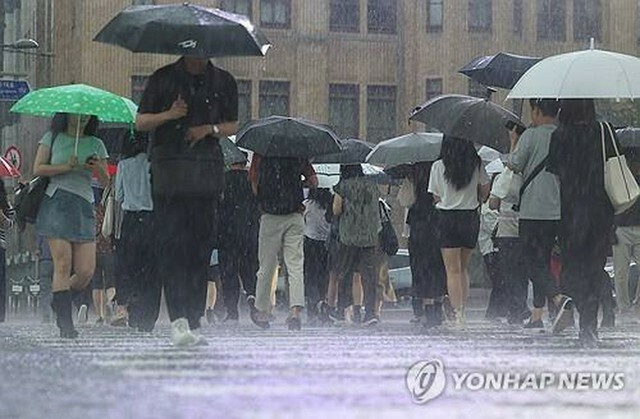 激しい雨が降る中、ソウル中心部の光化門広場付近を歩く人々＝17日、ソウル（聯合ニュース）