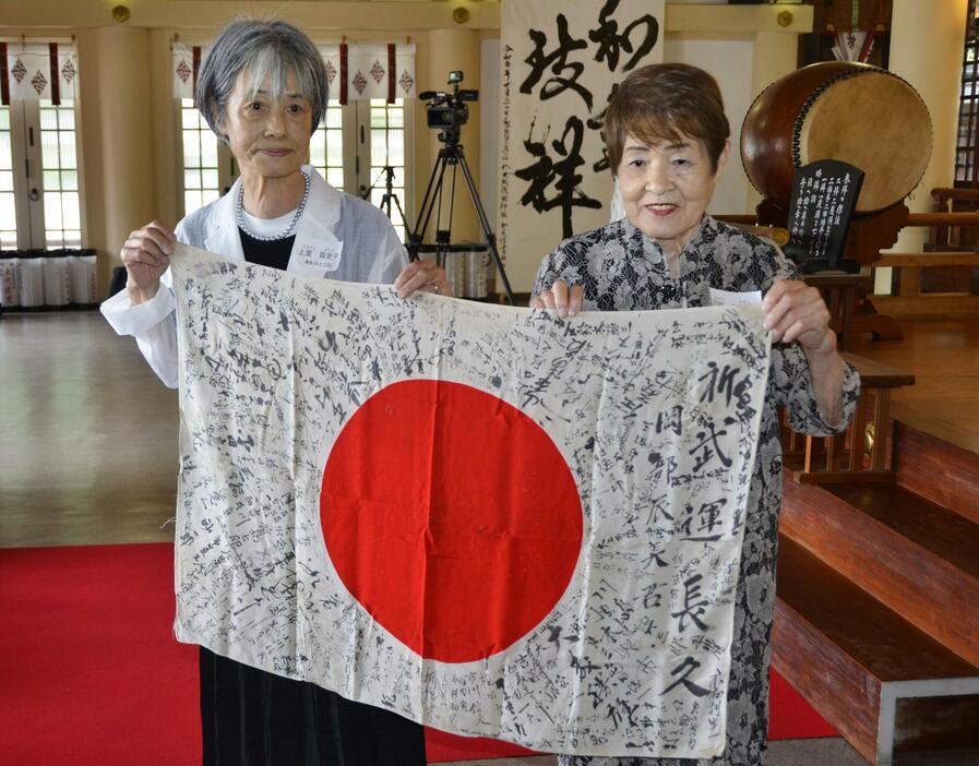 返還された岡部辰美さんの日章旗を掲げる長女の芙佐子さん（右）ら遺族＝14日、大阪市