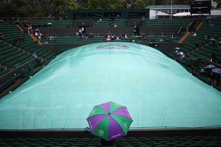 テニス、ウィンブルドン選手権。雨が降る中、カバーがかけられたコートを傘をさして見守る大会スタッフ（2024年7月9日撮影）。