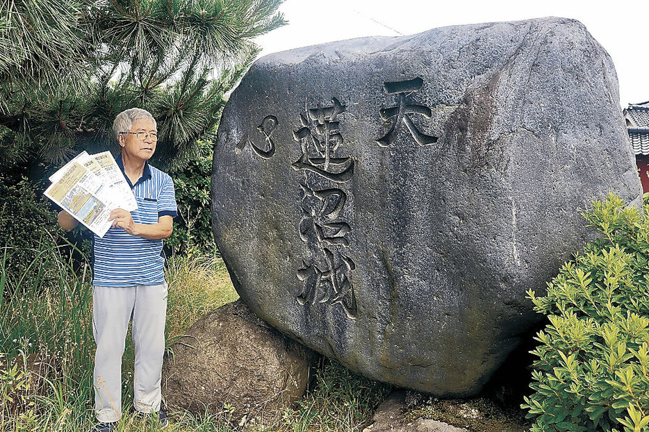 石碑の前でチラシを手に取る吉田さん＝小矢部市蓮沼