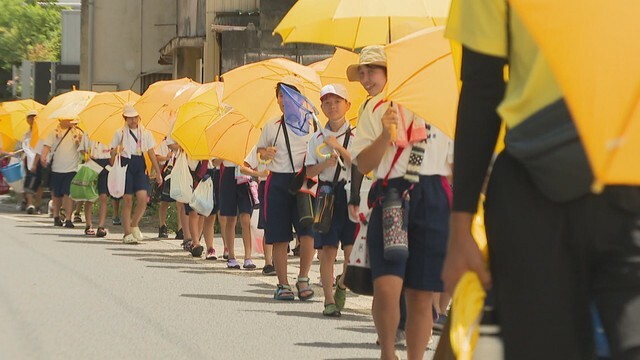 雨傘で日よけをする小学生