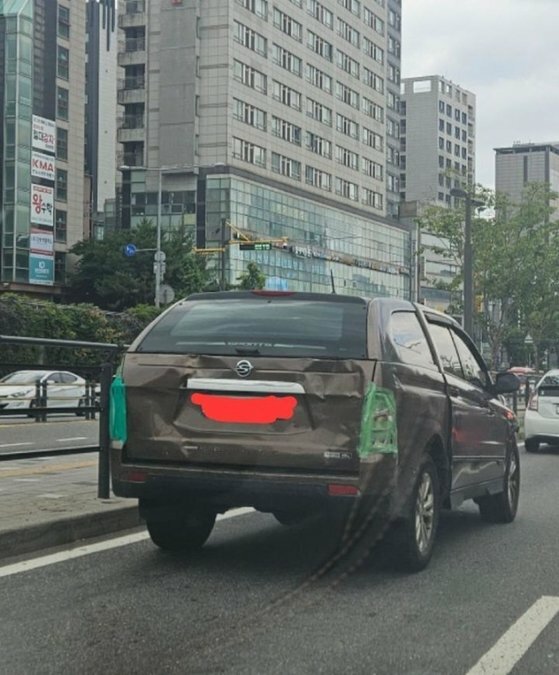 後面と側面がかなり凸凹し、バックライトに緑色のガムテープを張り付けたザ・ニュー・コランドスポーツ車両が路上を走行している。［写真　コミュニティ］