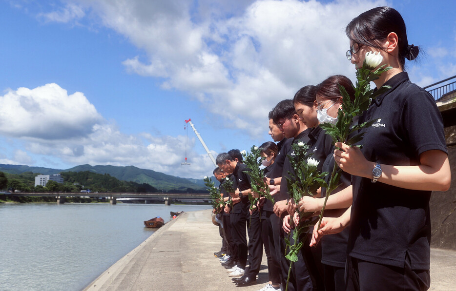 ４年前の熊本豪雨で氾濫した球磨川に向かい、花を手に黙とうする川下り船運航業者の従業員ら＝４日午前、熊本県人吉市