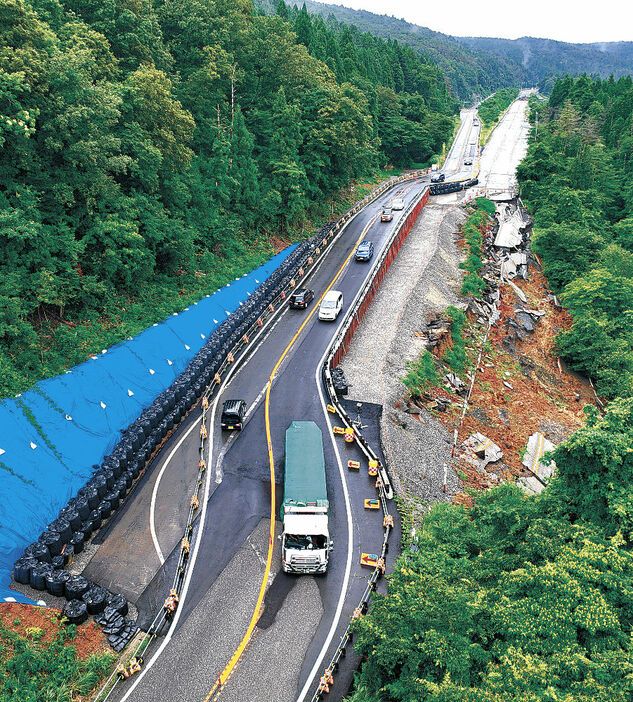 地震で崩れた本線脇に作られた迂回路を対面通行する車（下が金沢方面）＝１７日午後５時、のと里山海道横田ＩＣ付近（ドローンから）