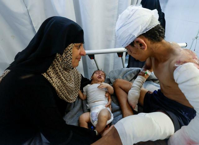 パレスチナ自治区ガザ南部ハンユニスの病院で2024年7月2日、イスラエル軍の空爆で負傷した赤ちゃん。母はこの空爆で死亡したといい、親類の女性に抱かれている。右の少年は赤ちゃんの兄=ロイター