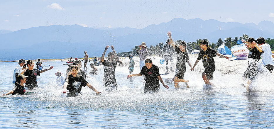 水しぶきを上げて海水浴を楽しむ若者＝富山市の岩瀬浜海水浴場