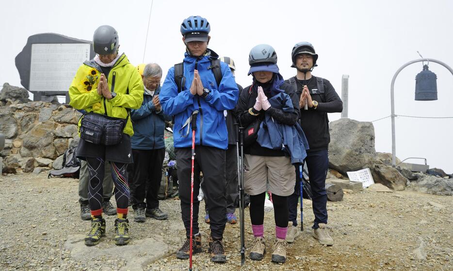 御嶽山の頂上で手を合わせて黙とうする遺族ら＝28日午前11時52分