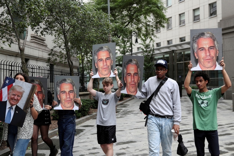 性的目的の少女の人身売買容疑で裁判にかけられた大富豪エプスタインの写真を掲げて抗議する人々（ニューヨーク）　REUTERS/Shannon Stapleton