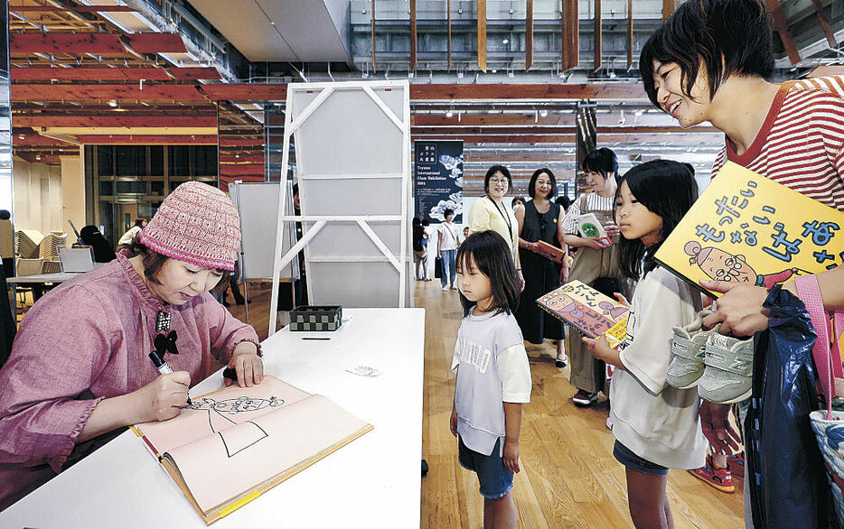 絵本にサインする真珠さん＝富山市立図書館