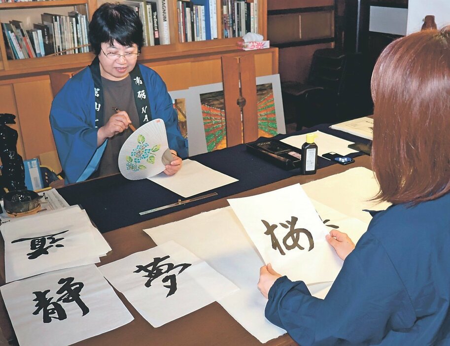 五箇山和紙に観光客が選んだ文字をしたためる書道有段者（左）