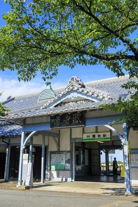 青空と緑葉が生い茂った桜の下で、水色の柱や屋根のドーマーが映える養老駅舎