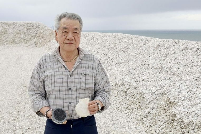 ホタテの貝殻でできた山の上に立つ「北栄」の小杉直司社長＝北海道八雲町