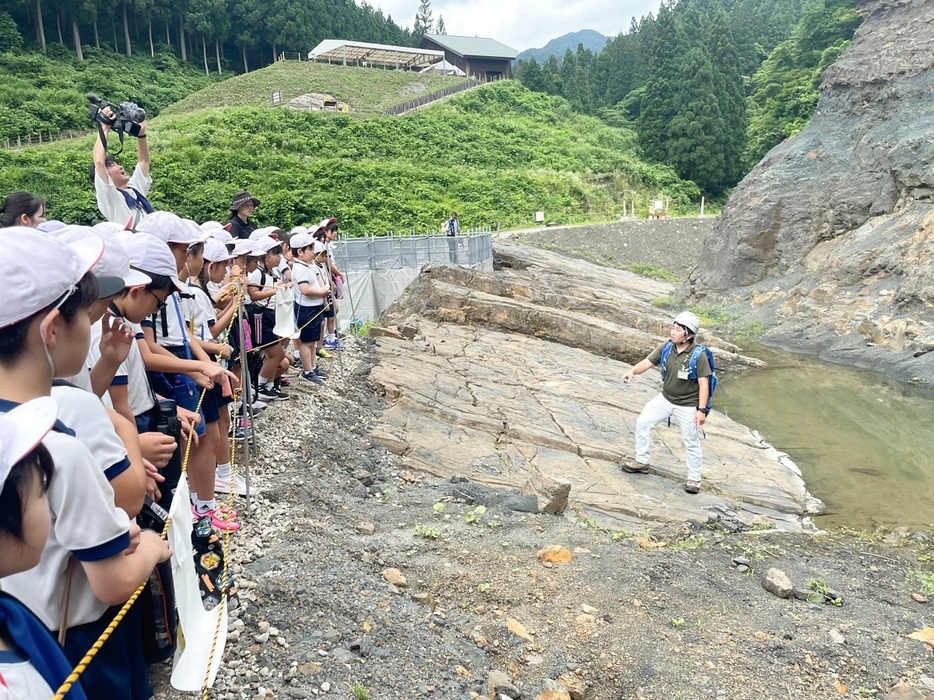 恐竜の化石などが発掘されている地層を間近で見学する児童ら＝7月19日、福井県勝山市北谷町杉山