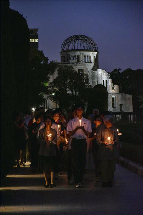 「ヒロシマ平和の灯のつどい」で、ろうそくを手に歩く人たち。後方は原爆ドーム＝31日夕、広島市の平和記念公園