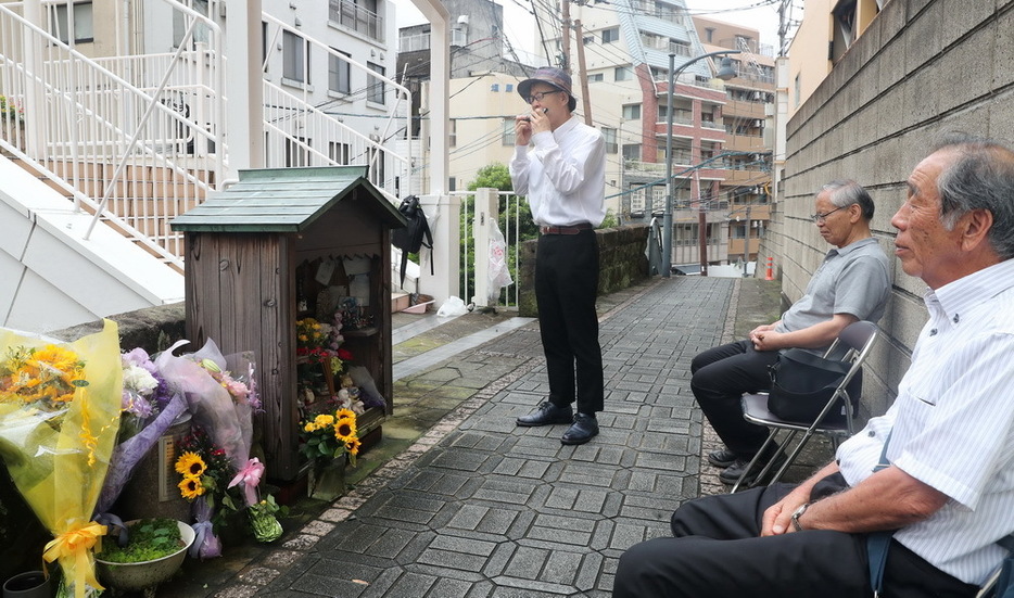 地蔵堂前でハーモニカを演奏する松尾さん（左）＝１日午前１０時１８分、長崎市万才町