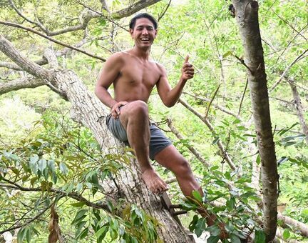 （資料写真）製作中のツリーハウスにある木の幹に腰をかけるキジーさん＝４月２２日、沖縄本島北部