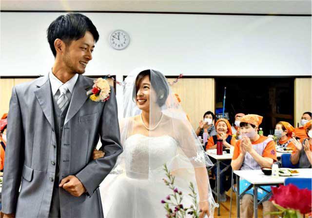 川南町山本地区の「おばちゃんたち」によるサプライズ結婚式に笑顔を浮かべ入場する（手前左から）佐師輝洋、香恋さん夫婦＝１３日午前、同地区コミュニティセンター