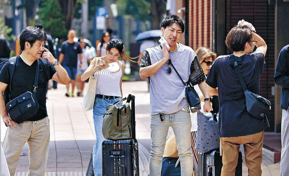 汗を拭いながら歩く人々＝１８日午前１１時、金沢駅前