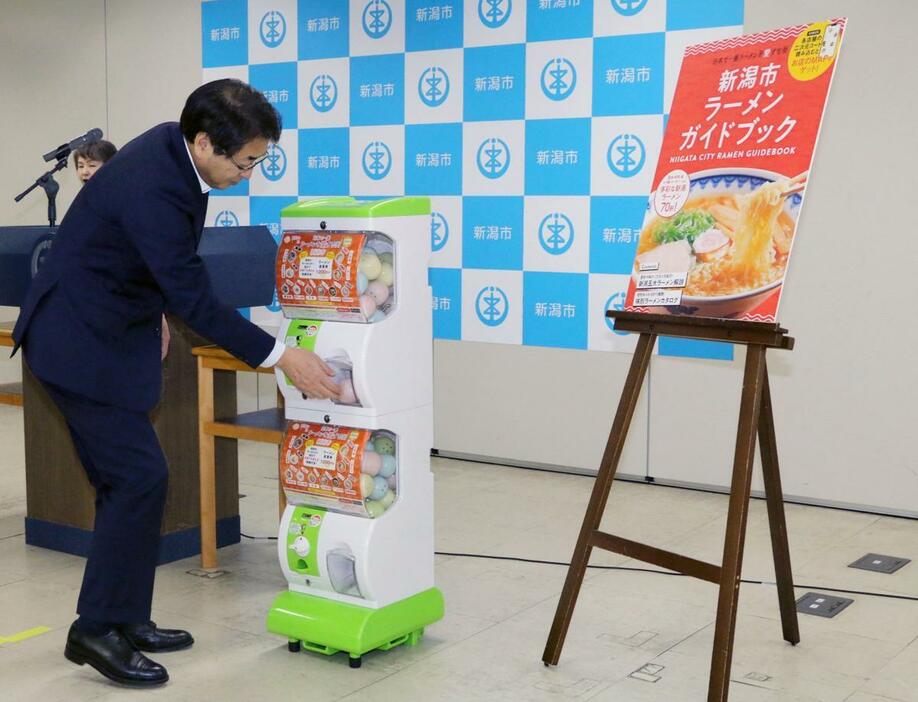 ラーメンのキーホルダーが入った街ガチャを回す中原八一・新潟市長=7月19日、新潟市役所