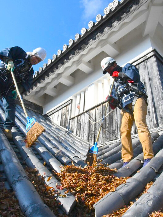 天守の屋根にたまった落ち葉を掃除する作業員