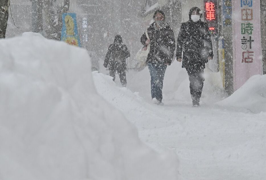 断続的な雪の中、脇に雪の山ができた歩道を行き交う市民＝27日午後、青森市古川2丁目