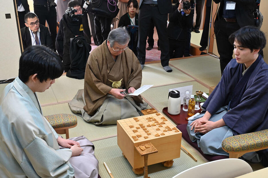 佐々木勇気八段（右）、藤井聡太竜王（左）が見守る中、立会人の青野照市九段（中央）が佐々木の封じ手を封筒を開封（日本将棋連盟提供）