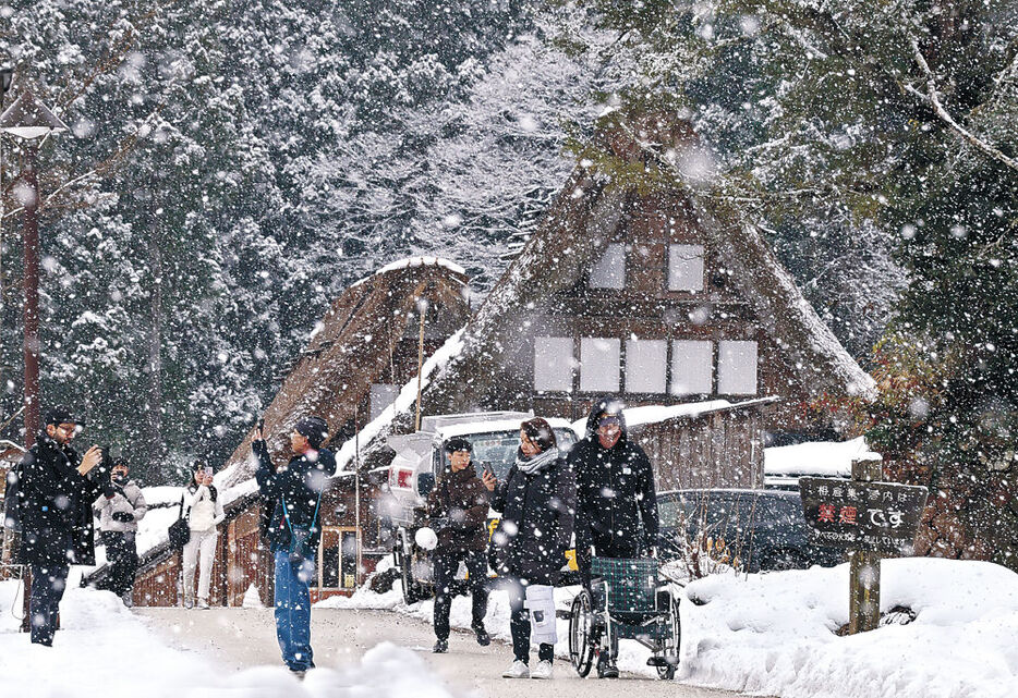 降りしきる雪の中、集落を散策する外国人観光客＝南砺市の相倉合掌造り集落