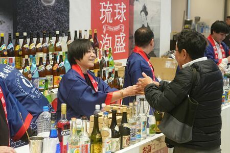 県内45カ所の酒造所の泡盛が飲めるイベントで、コップに注がれた泡盛を来場者に手渡すスタッフ＝19日、那覇市・タイムスビル（竹花徹朗撮影）