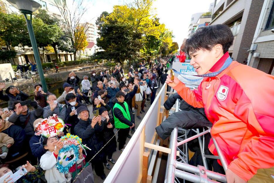 メダルを手に沿道の声援に応える岡選手＝8日午後1時26分、岡山市北区