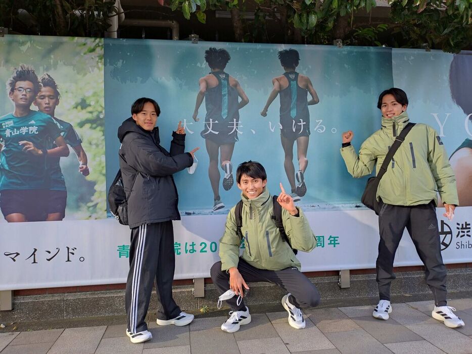 最初で最後の箱根駅伝に臨む青学大の鶴川正也（右）は、青山キャンパス前に掲げられた巨大な応援横断幕の前で力強くガッツポーズ（左は塩出翔太、中央は田中悠登主将）＝カメラ・竹内　達朗