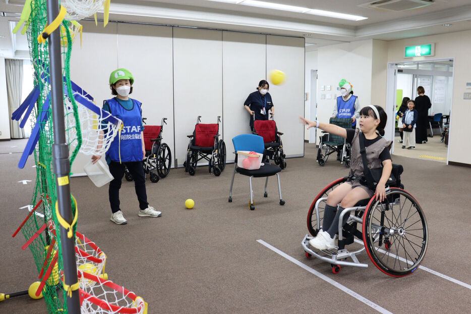 競技用車いすに乗り、ミニバスケットゴールを目がけてボールを投げる子ども（向日市寺戸町・市福祉会館）