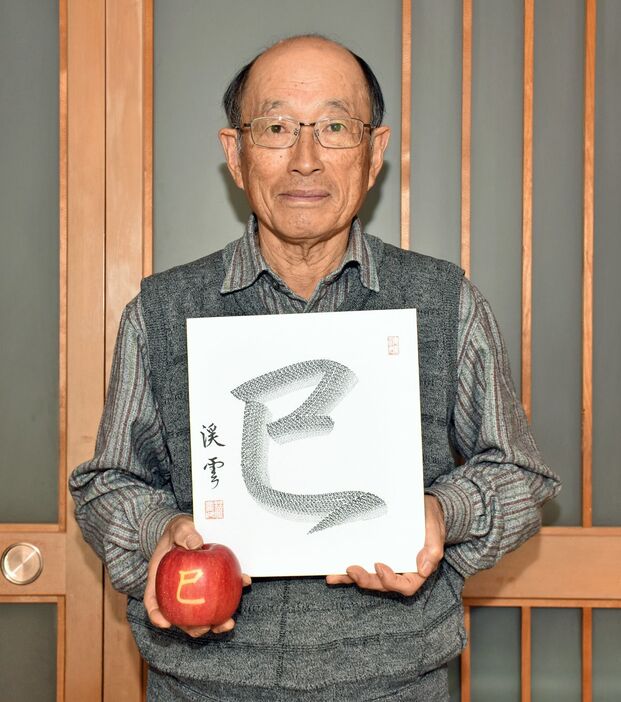 1245字で描いた「巳」と自作の文字入りリンゴを手にする小笠原さん