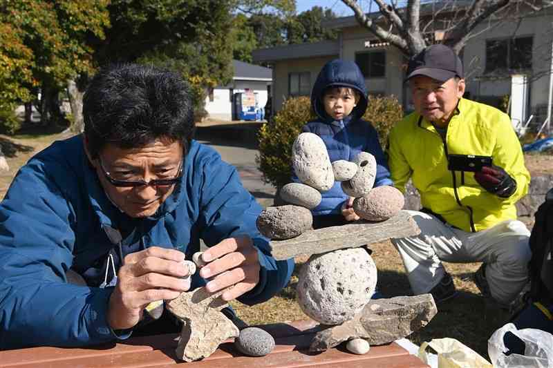 「ロックバランシング」に没頭する佐藤清貴さん（左）。散歩する家族連れも興味津々＝19日、熊本市東区の江津湖畔（小野宏明）