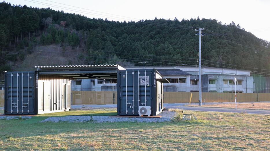 震災遺構となった大川小の校舎（奥）北側の空き地に立つ「Team大川　未来を拓くネットワーク」のコンテナ事務所＝10日午後、宮城県石巻市