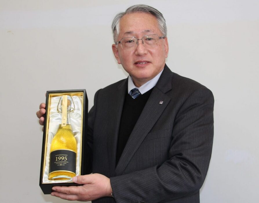 西向賞雄・取締役製造部部長。「1995年醸造 生酛純米古酒」を手に「豚の角煮や中華料理などと相性が良いと思います」＝2024年12月11日午後、神戸市中央区