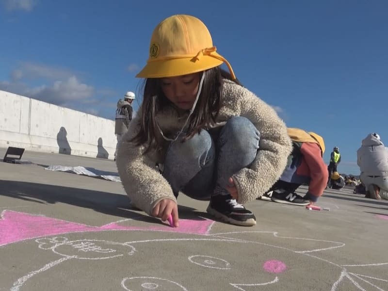 開通前の道路にチョークで絵を描く児童＝９日午前、本巣市内、本巣ＰＡ付近