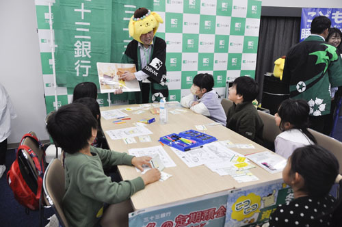 【銀行の役割を紙芝居で学ぶ子どもら＝鈴鹿市飯野寺家町の市文化会館で】