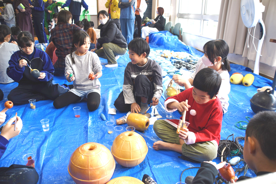 筆を使って浮きに絵の具を塗る参加者ら＝21日、鹿児島県宇検村平田