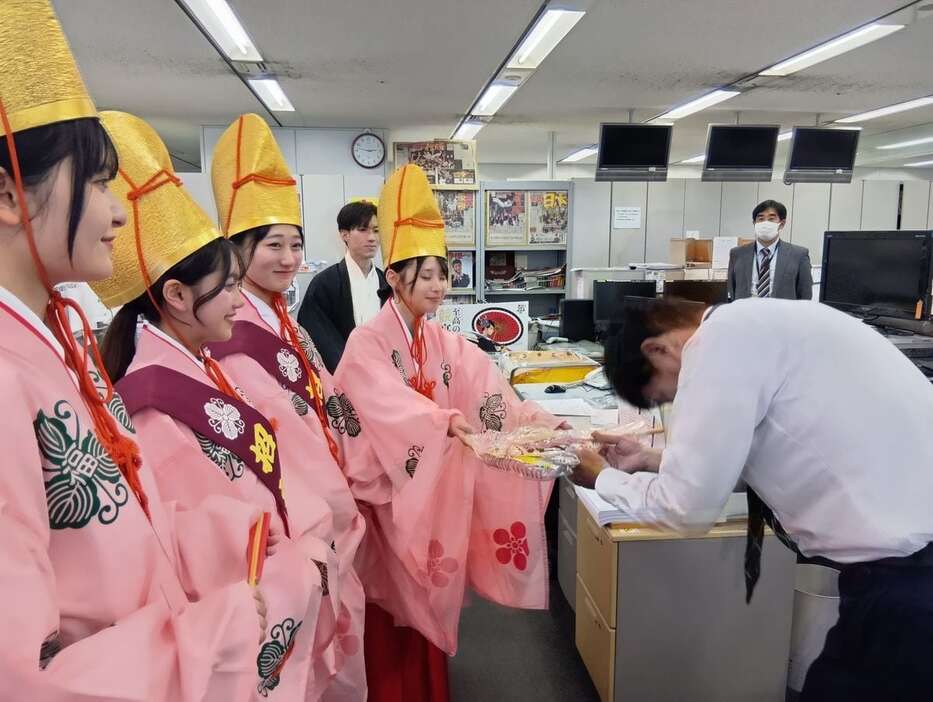 福娘から縁起物を授かる矢田整理部長（右）。学問の神様であり、ギャンブルの神様ではないが…