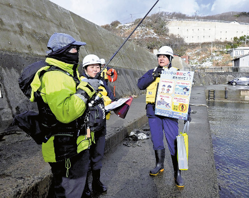 門前漁港で釣りをする人（左）に注意喚起をする秋田海保の職員（１８日、男鹿市で）