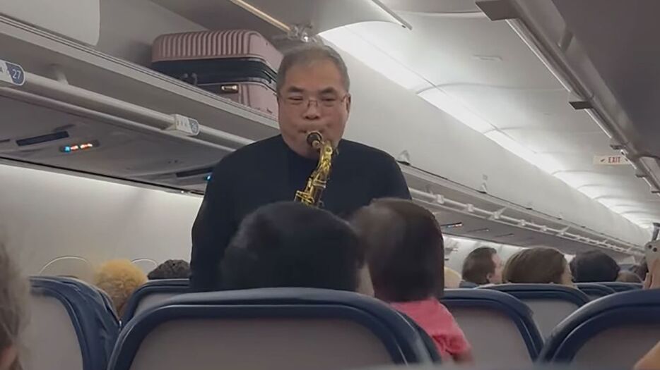 旅客機の機内でクリスマスソングを演奏するウェイン・ホーイさん