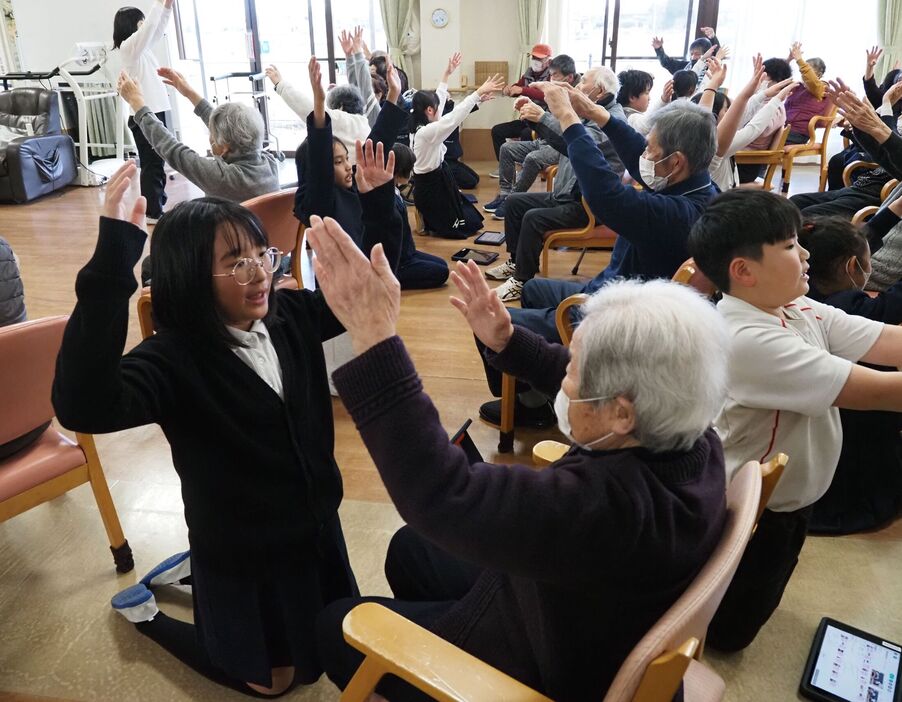 音楽に合わせて一緒に常盤健康体操を行う児童とお年寄りら（草津市志那中町・常輝の里）