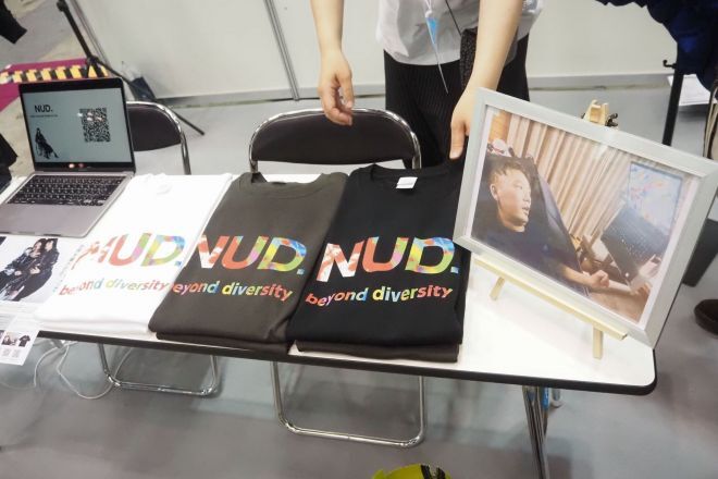 国際福祉機器展のブースで展示されたTシャツと視線入力で絵を描く男性の写真＝朝日新聞社