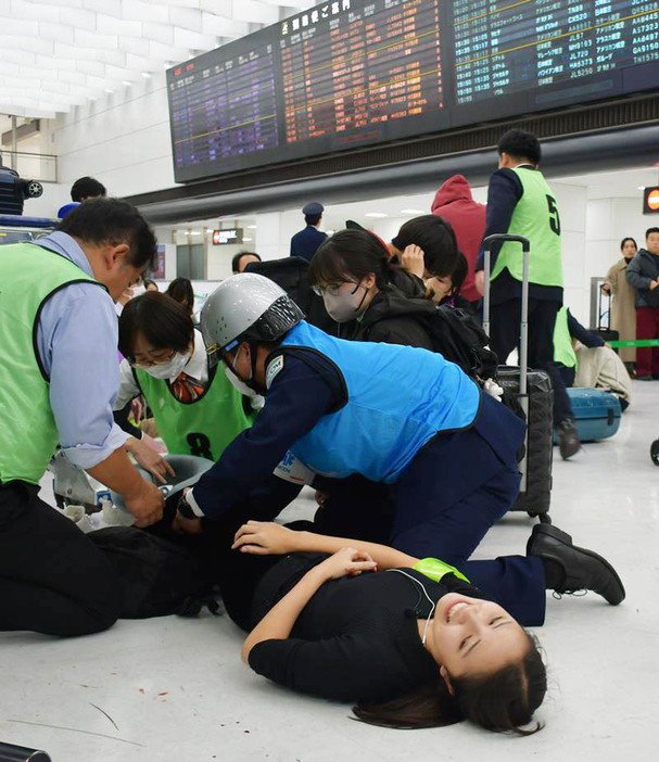 足に重傷を負った成田空港の旅客を演じる学生を救護する訓練参加者ら