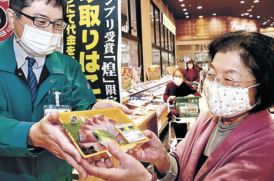 「煌」の刺し身を受け取る来店客＝３日午前９時４５分、七尾市内の食品スーパー