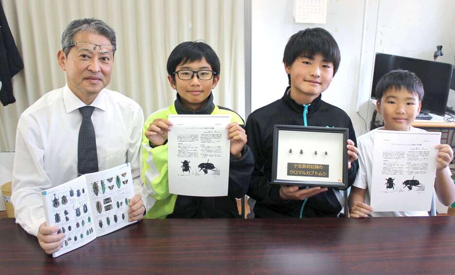 小宝島で初確認となったクロマルカブトムシの標本などを手にする小宝島学園生と牧野忠彰校長（同学園提供）