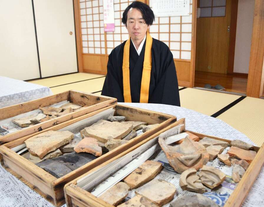 焼けた瓦片と、発見者の松元章徳さん＝都城市牟田町