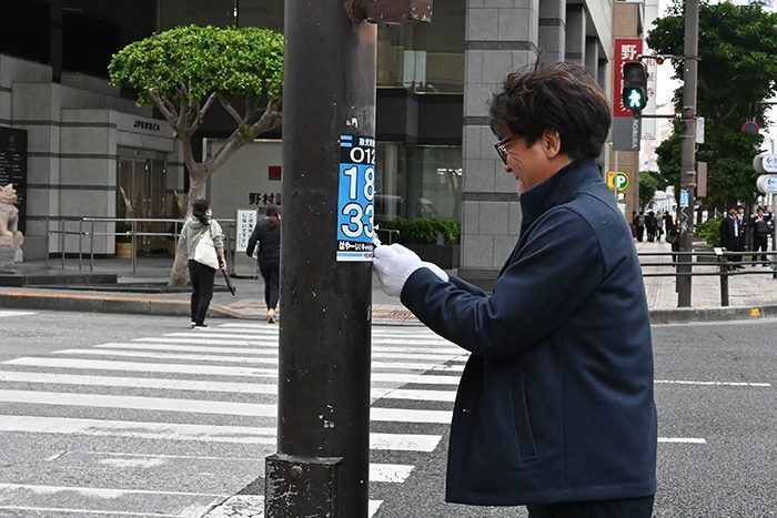 ヤミ金融の連絡先とみられる電話番号が書かれ電柱に貼られた広告物をはがす司法書士の安里長従さん＝26日、那覇市久茂地