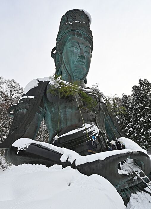 頭や肩に雪をかぶった昭和大仏。青龍寺の関係者がすす払いを行った＝15日午前、青森市桑原